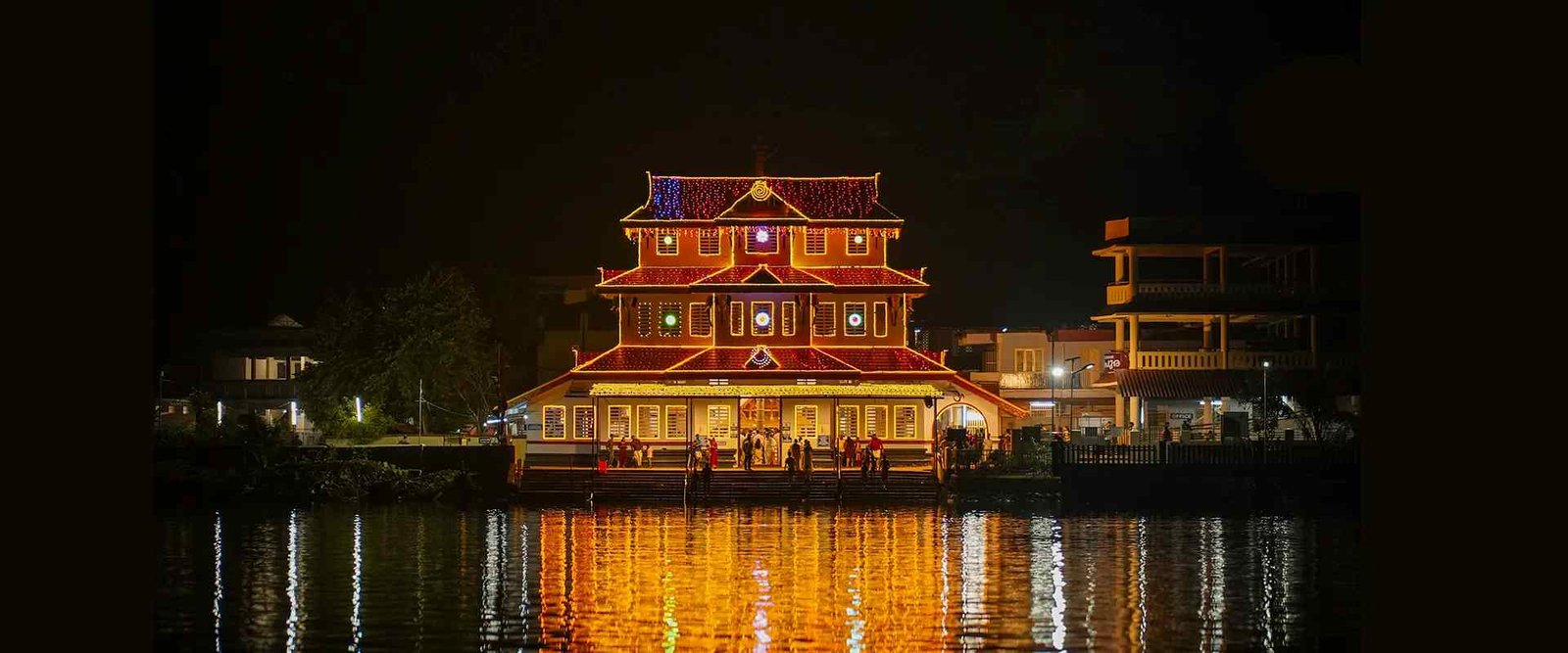 Parassinikadavu Muthappan Temple beautifully illuminated at night with reflections in the river.