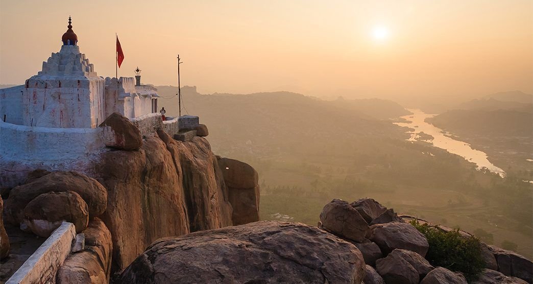 Sunrise view of Yantrodharaka Hanuman Temple on a rocky hill in Hampi with the Tungabhadra River below.